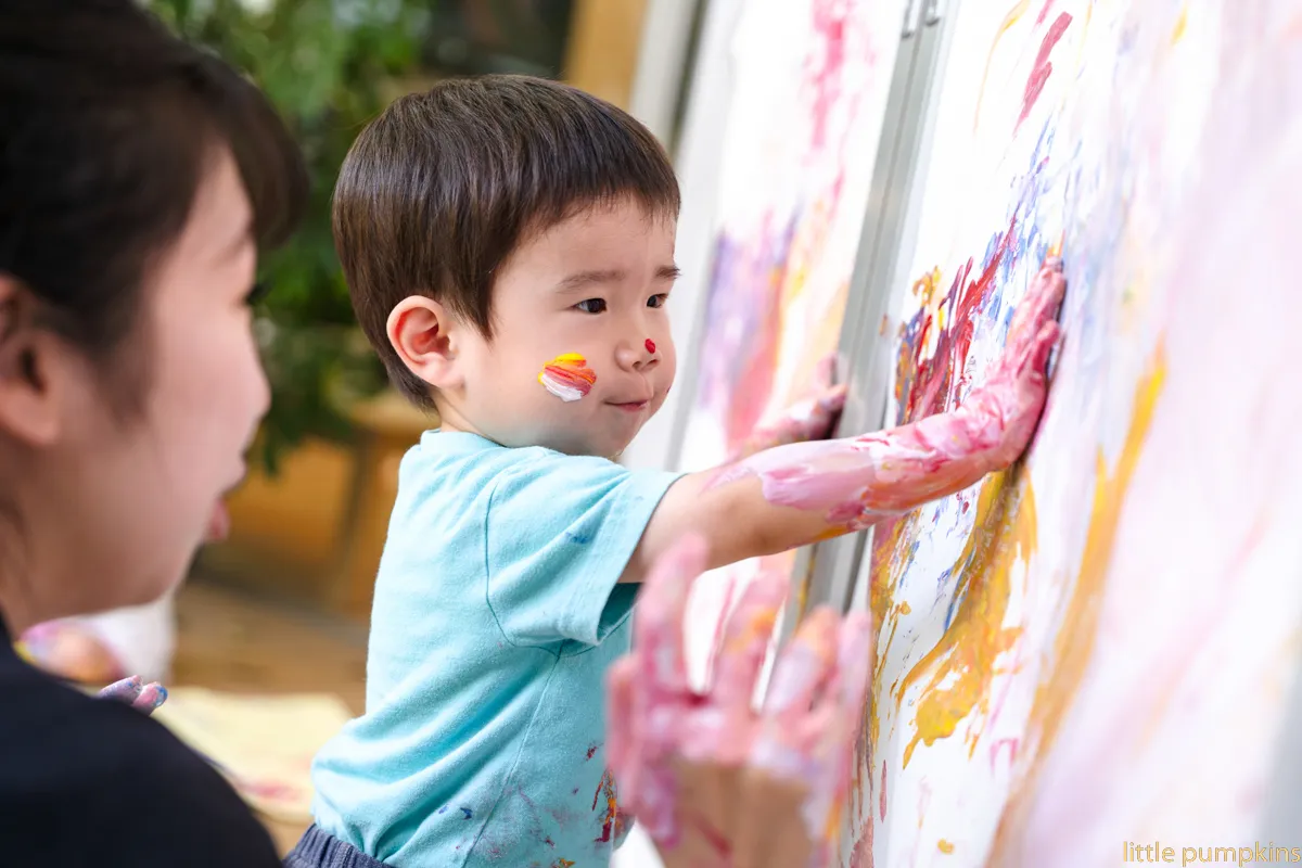 子供が顔や手に絵の具をつけて壁に絵を描いて遊んでいる様子