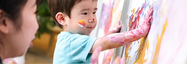 保育士と園児が一緒に指画用の絵の具で遊んでいる様子