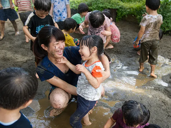 泥だらけになりながら、笑顔で楽しく遊ぶ保育士と園児の様子