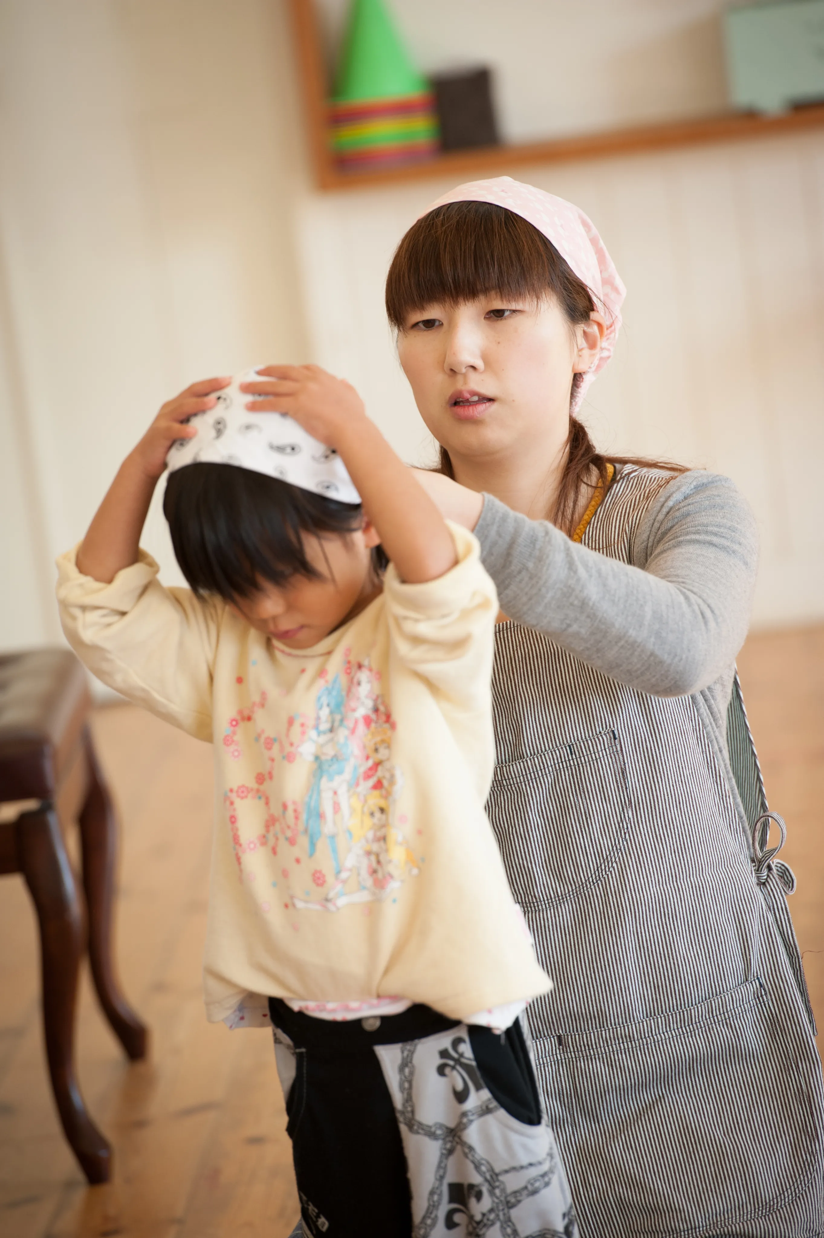 保育士が園児の頭にバンダナを巻くのを手伝っている様子